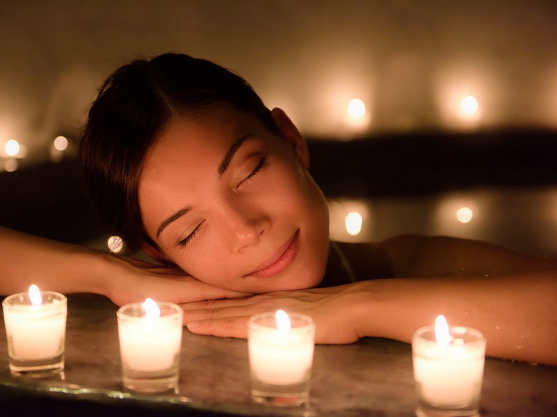 Beautiful young woman relaxing in jacuzzi hot tub at spa. Attractive female tourist is surrounded with lit candles. Smiling woman with eyes closed is pampering herself during vacation.